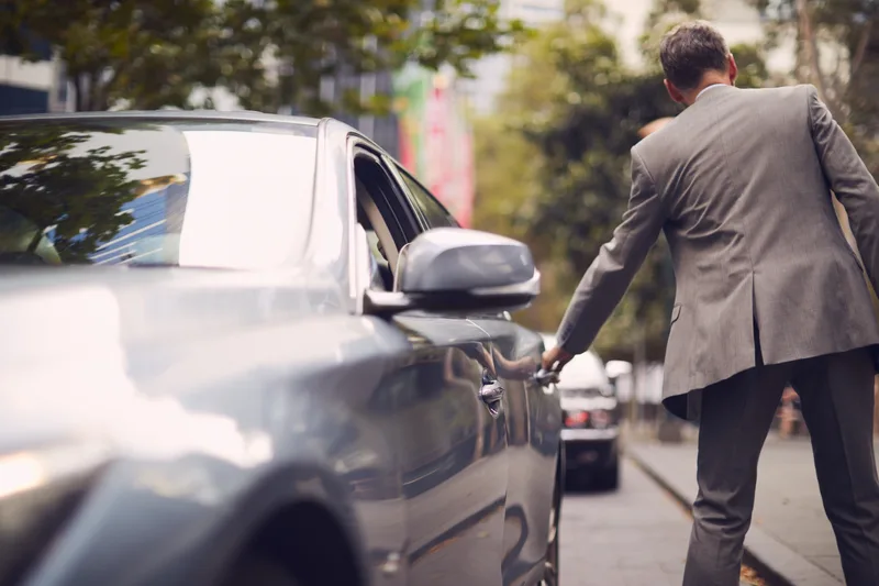 A chauffeur opening the rear door of a luxury car on a city street