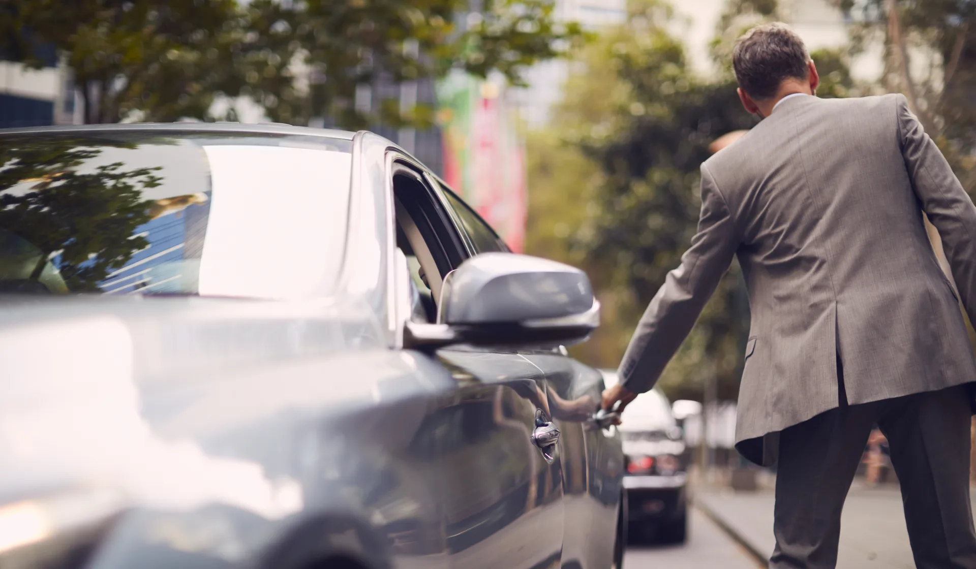 A chauffeur opening the rear door of a luxury car on a city street