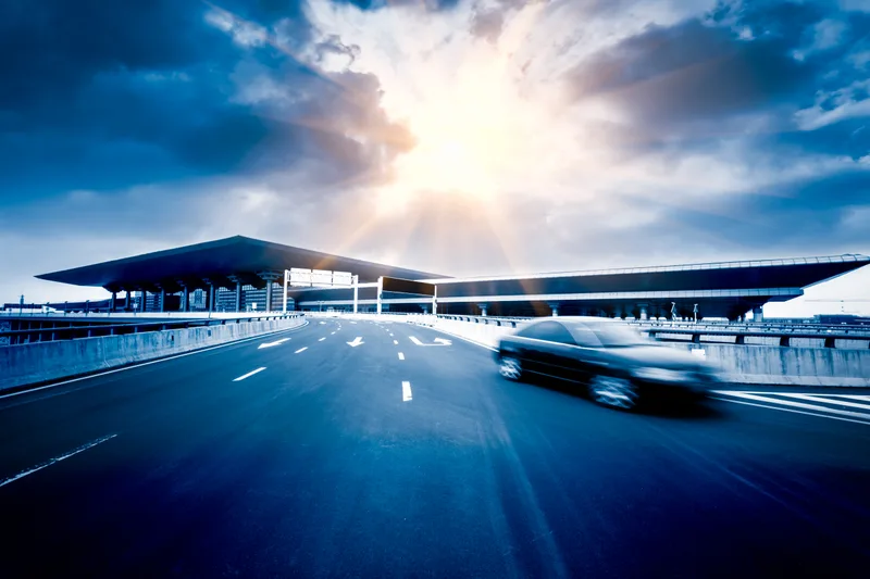 A chauffeured black car outside the airport terminal at dusk