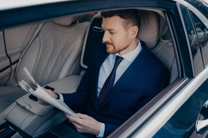 A passenger relaxing in the back seat of a chauffeured car