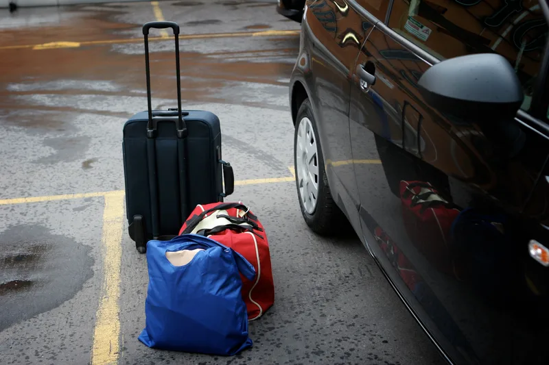 A traveller's luggage being loaded into a car at the airport curb