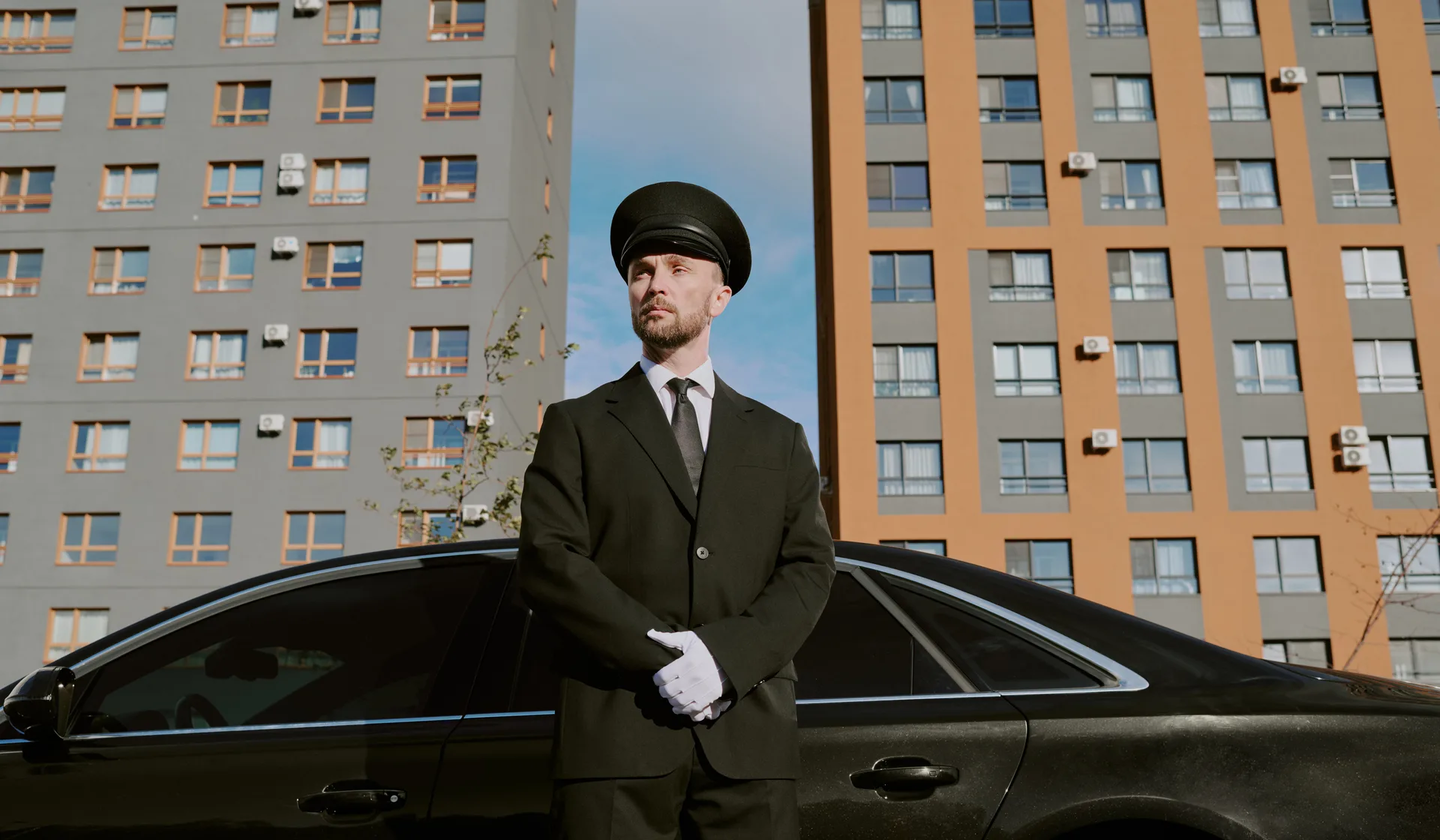 A chauffeur waiting beside a luxury car in the city